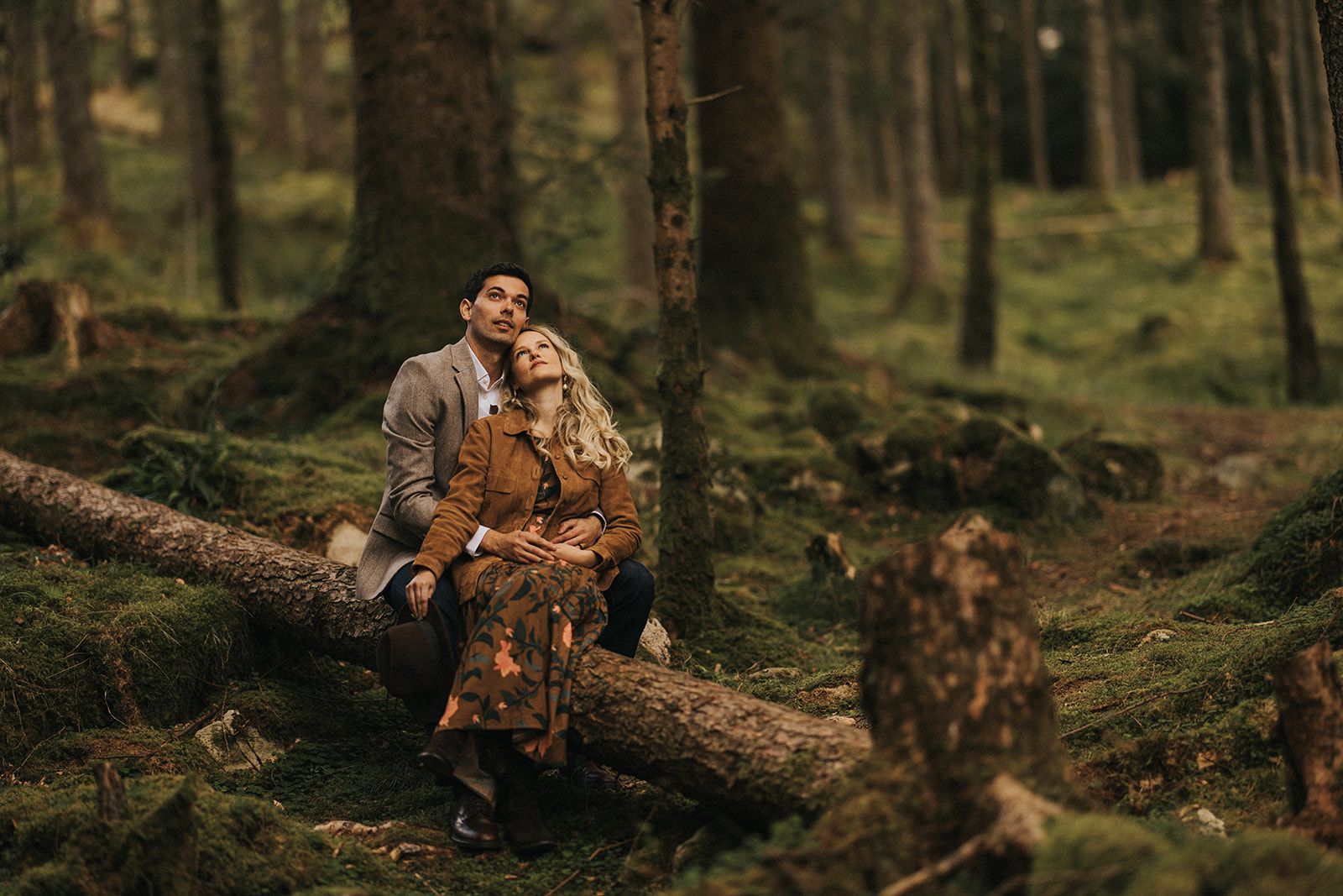 Figure sitting on fallen log in atmospheric misty forest wearing brown outdoor clothing during autumn season.