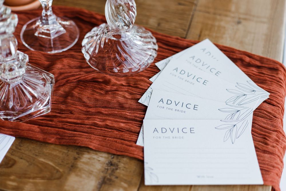 White paper advice cards arranged on a rustic wooden table at a bridal shower.