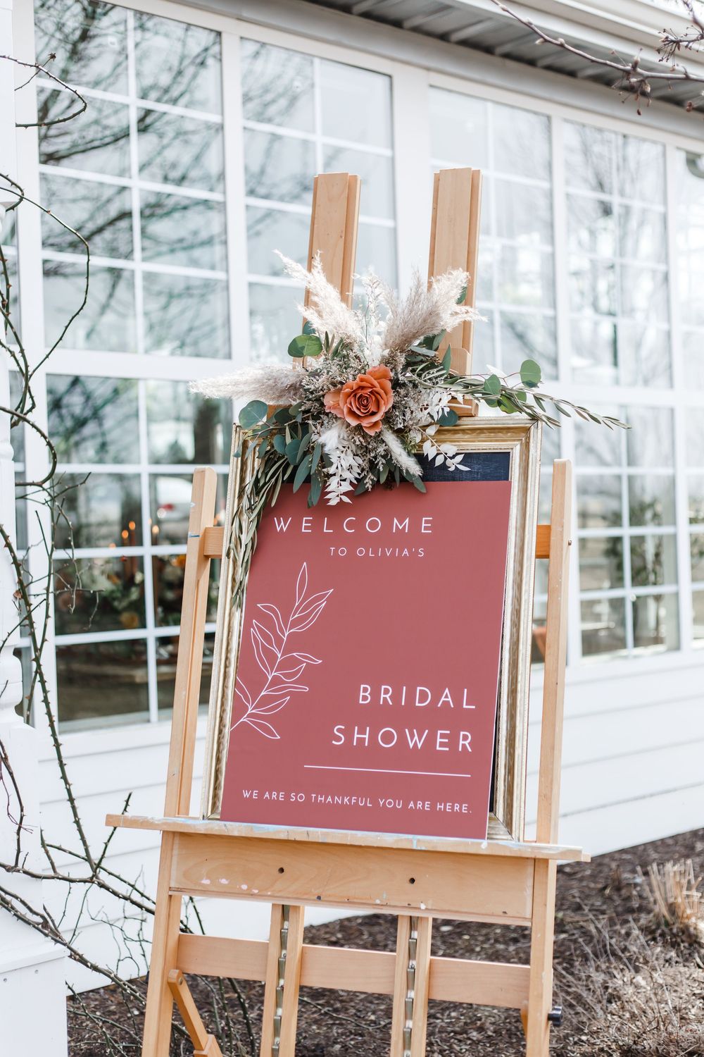 Terracotta-colored welcome signs on wooden easels adorned with floral decorations for a bridal shower.