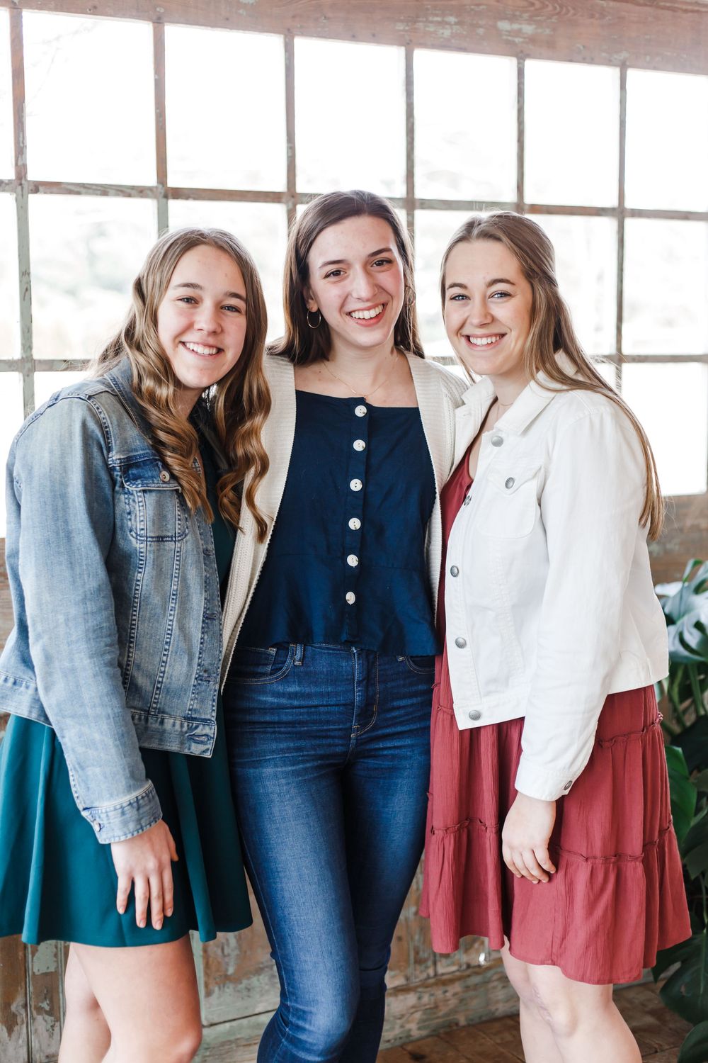 Group posed in casual denim and spring outfits in front of industrial windows.
