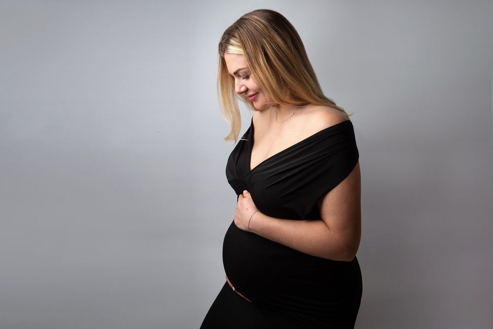 Elegant maternity portraits in grey tones showing a pregnant figure in black attire.