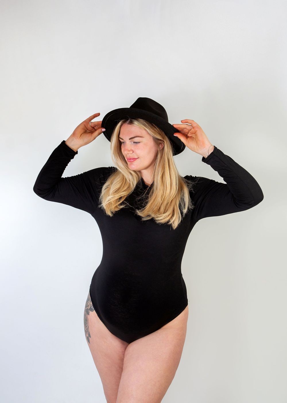 Fashion-forward maternity shoot with model in black bodysuit and hat striking dynamic poses.