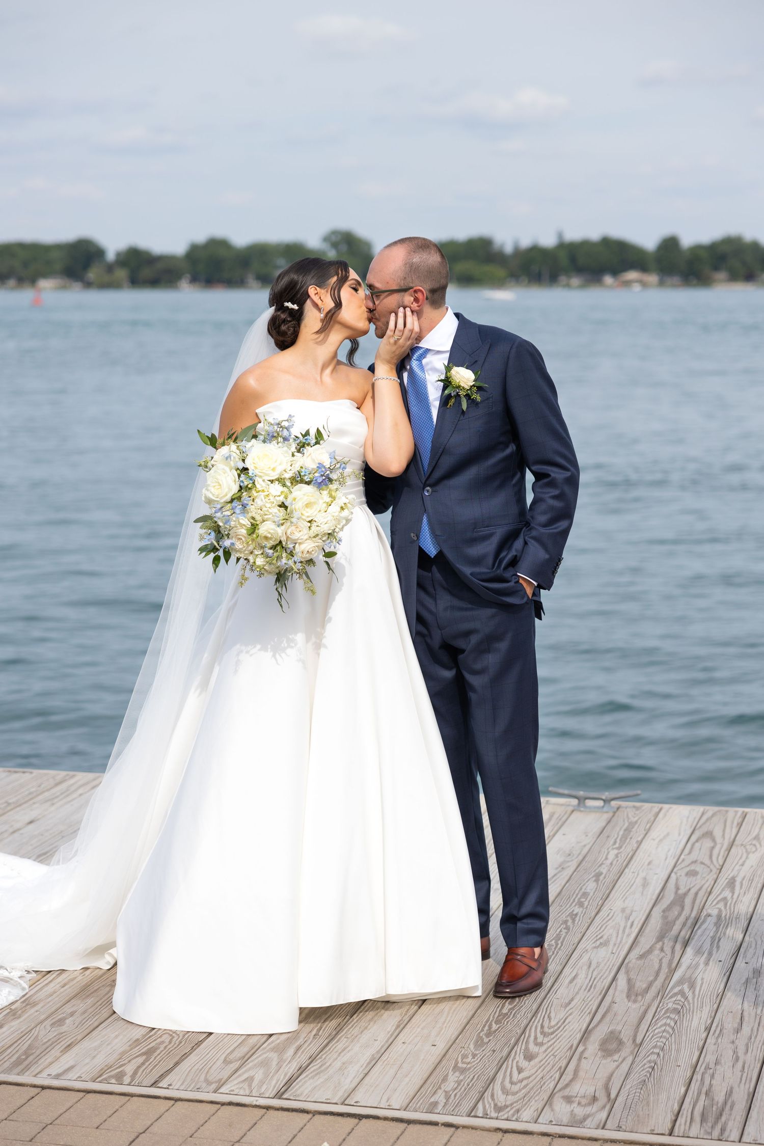A wedding couple shares an intimate moment on a wooden dock overlooking a serene lake on their special day. SE Michigan wedding photographer