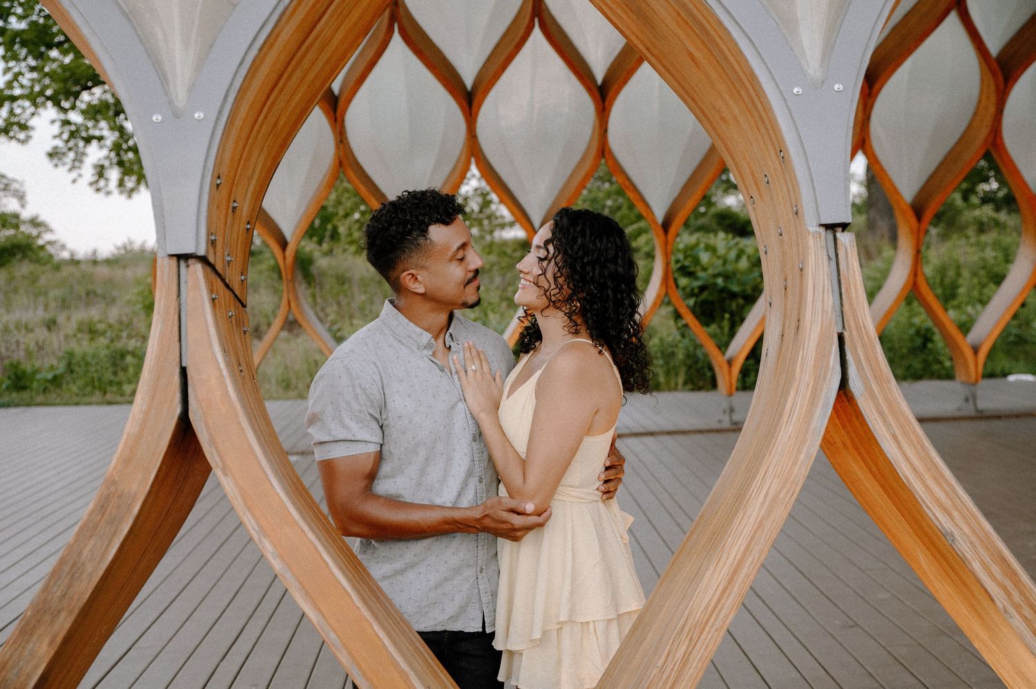 Couple shares romantic moment through heart-shaped wooden architectural feature in outdoor garden setting.