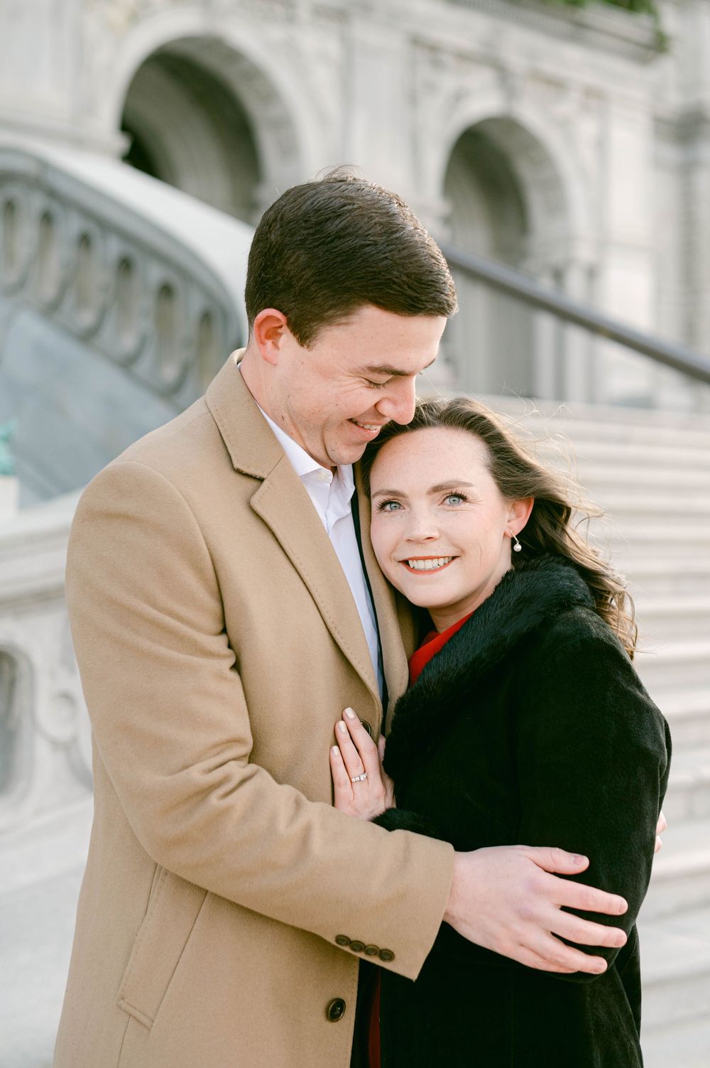 A winter engagement photo featuring a couple in warm coats embracing on stone steps.