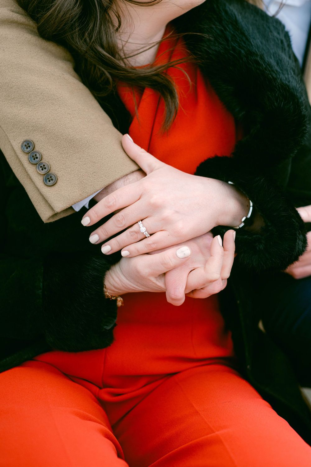 Close-up of hands displaying an engagement ring against a red dress backdrop.