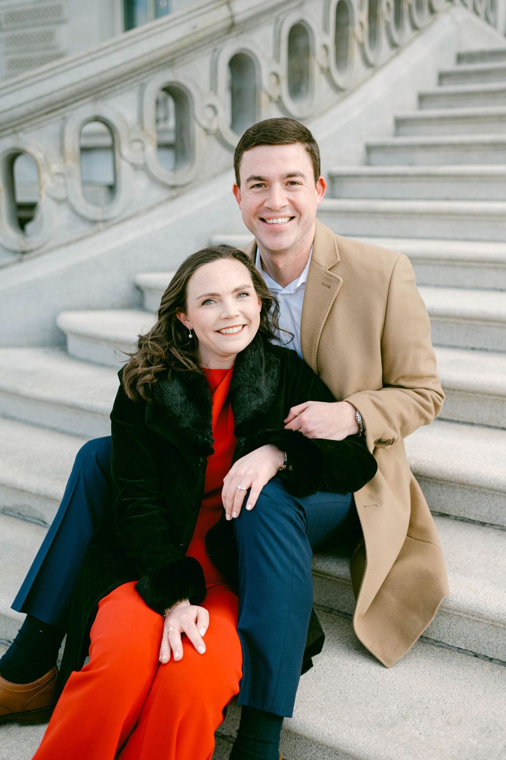 Happy couple posing together on elegant white stone steps with ornate architecture.