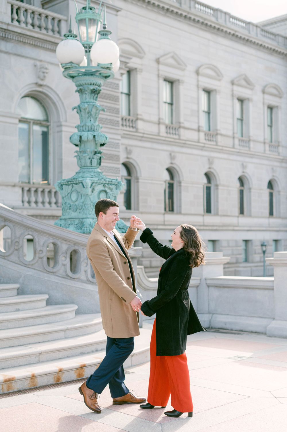 Playful couple dancing and spinning on marble steps with decorative lampposts.