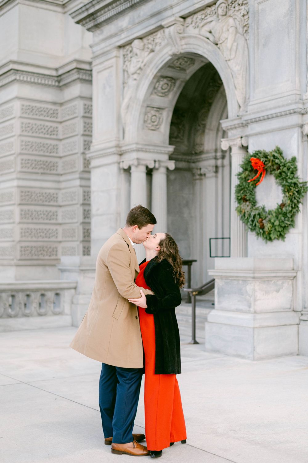 Couple sharing romantic moment near holiday wreaths on classical building facade.