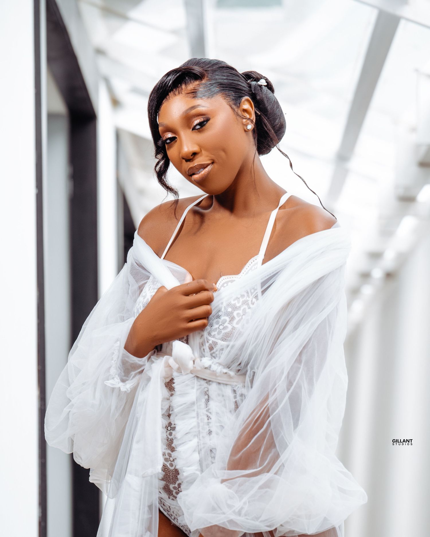 Portrait of model wearing white lace lingerie and sheer robe in bright modern setting.