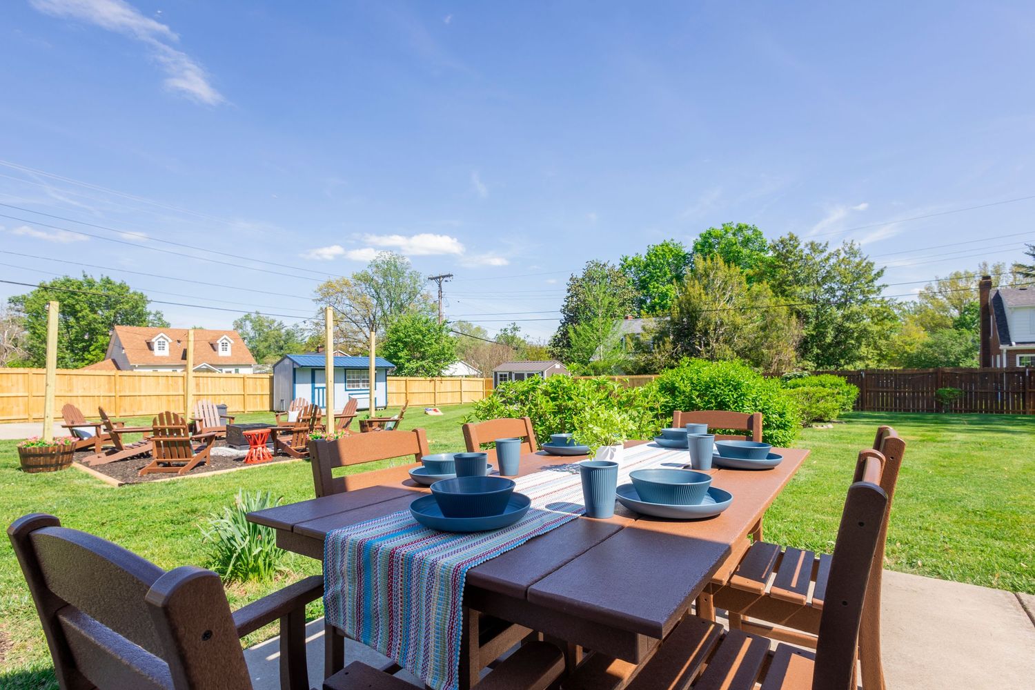 Outdoor dining table set on backyard patio with green lawn and residential homes in background.