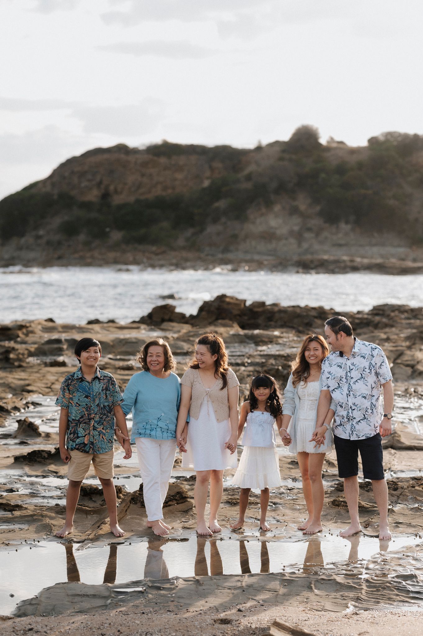 A group walks along a rocky coastal shoreline at sunset wearing coordinated blue and white casual outfits.