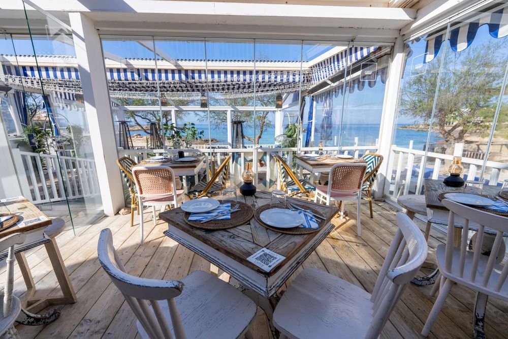 Coastal dining terrace with elegant table settings and white chairs under a covered patio with ocean views.