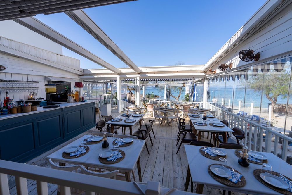 A bright waterfront restaurant with white decor and outdoor dining terrace overlooking the ocean and beach view.