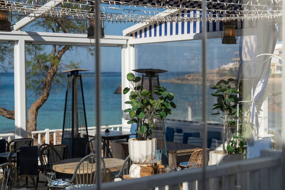 Modern oceanfront restaurant patio with white columns and glass panels offering panoramic views of the sea and coastline.