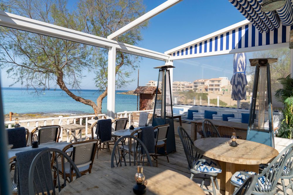 Beachfront Mediterranean restaurant terrace with blue and white decor, patio heater, and ocean view seating.