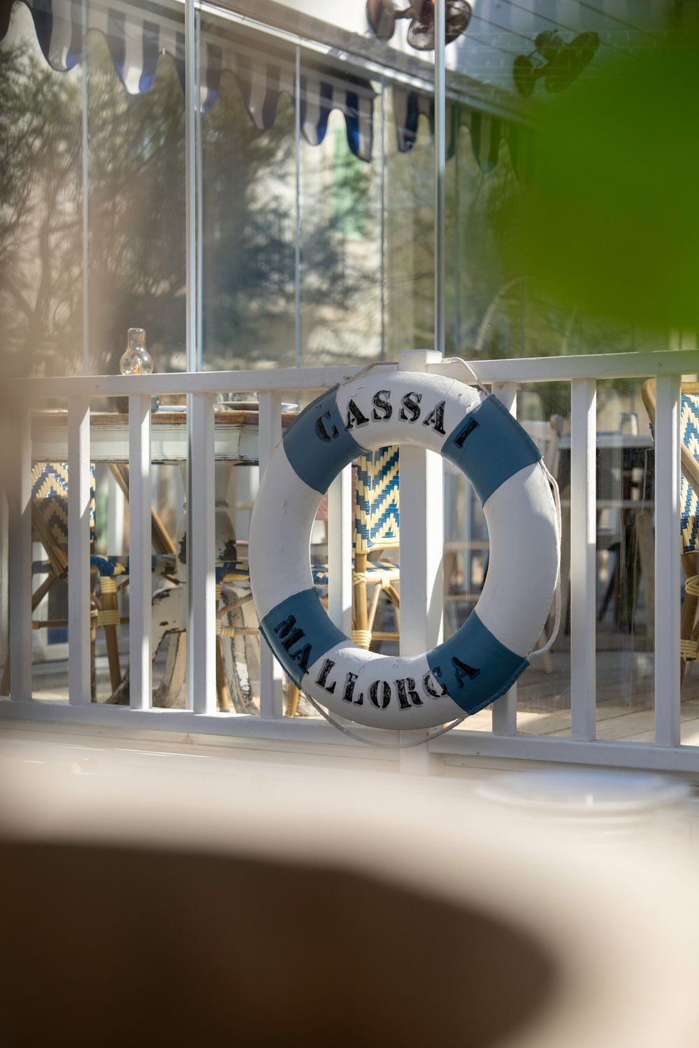 A white and blue nautical life preserver ring with 'Massa' and 'Mallorca' text hangs on a white railing in sunlight.