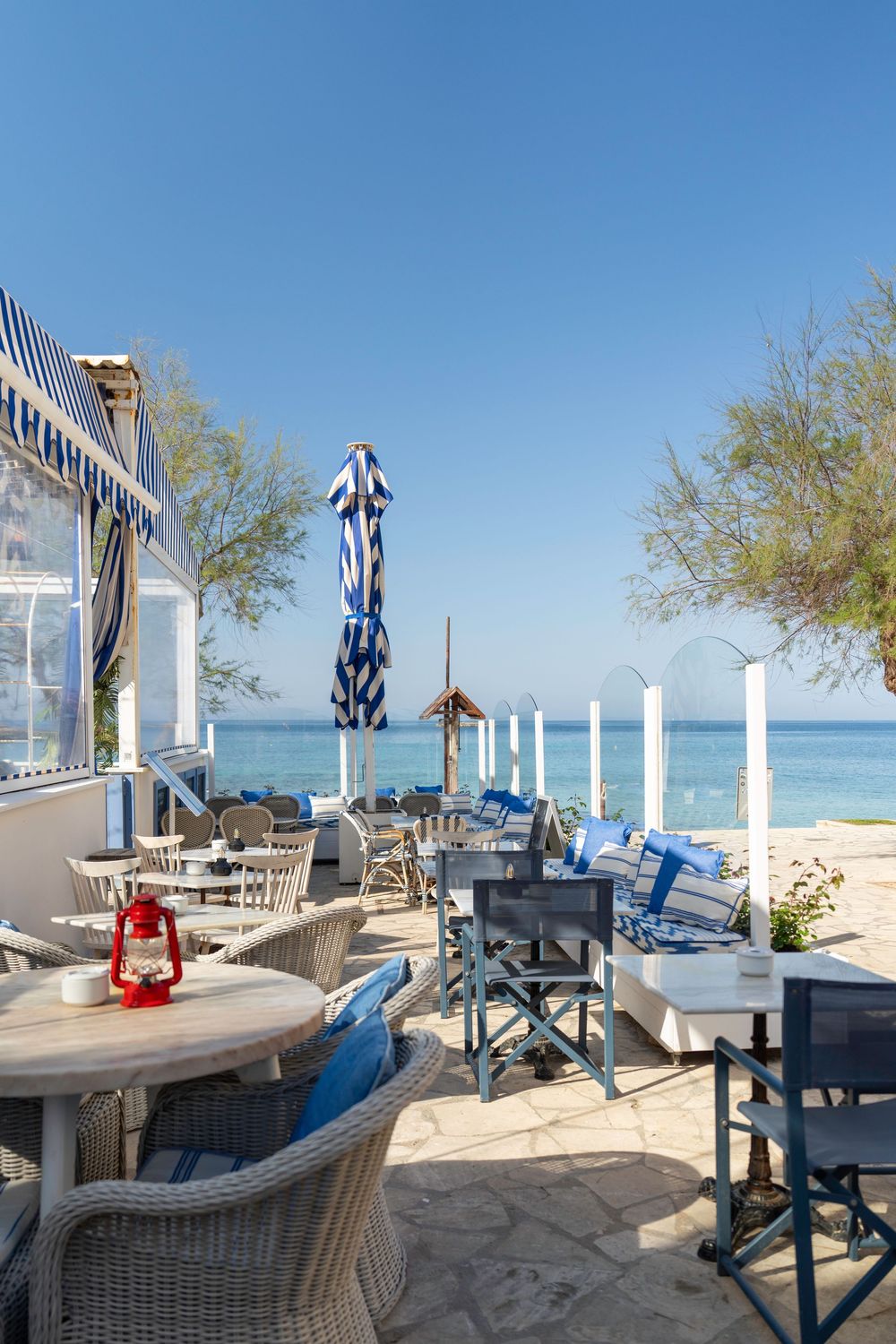 Beachfront restaurant patio with wicker furniture, blue striped umbrellas and ocean views along a wooden deck.