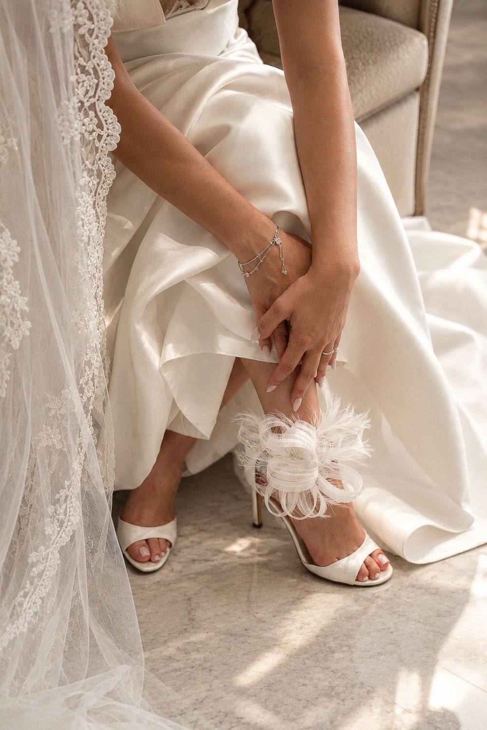 Close-up of bride adjusting white feathered heels while seated in her satin wedding gown in Valle de Guadalupe, Baja.