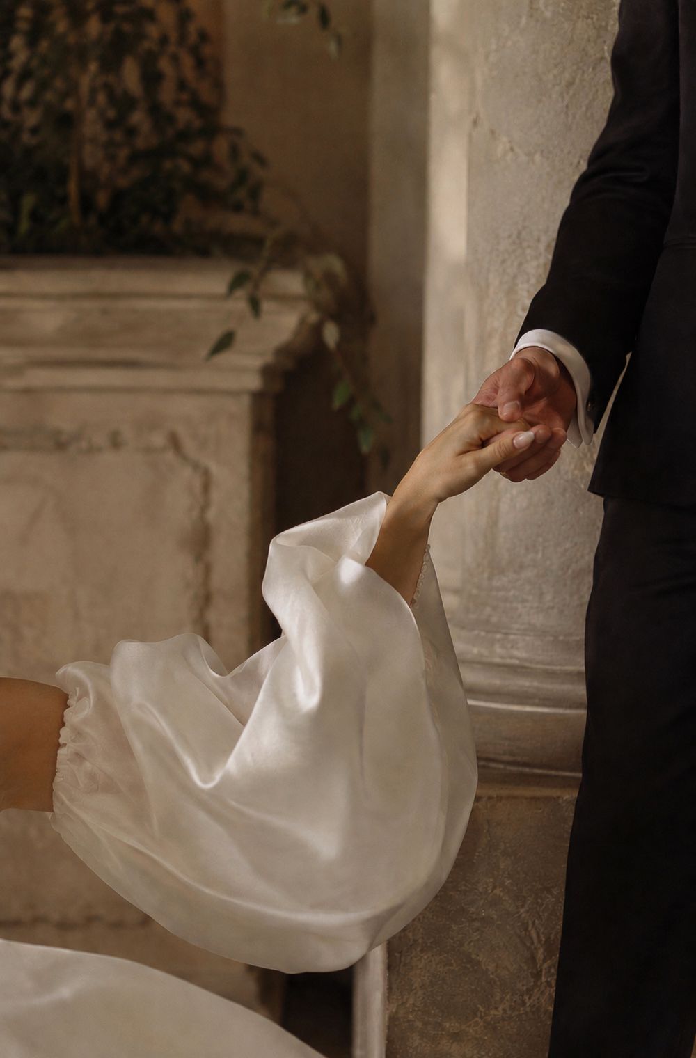 Bride and groom holding hands by a stone wall, with the bride in a flowing satin gown, at their wedding in Valle de Guadalupe.