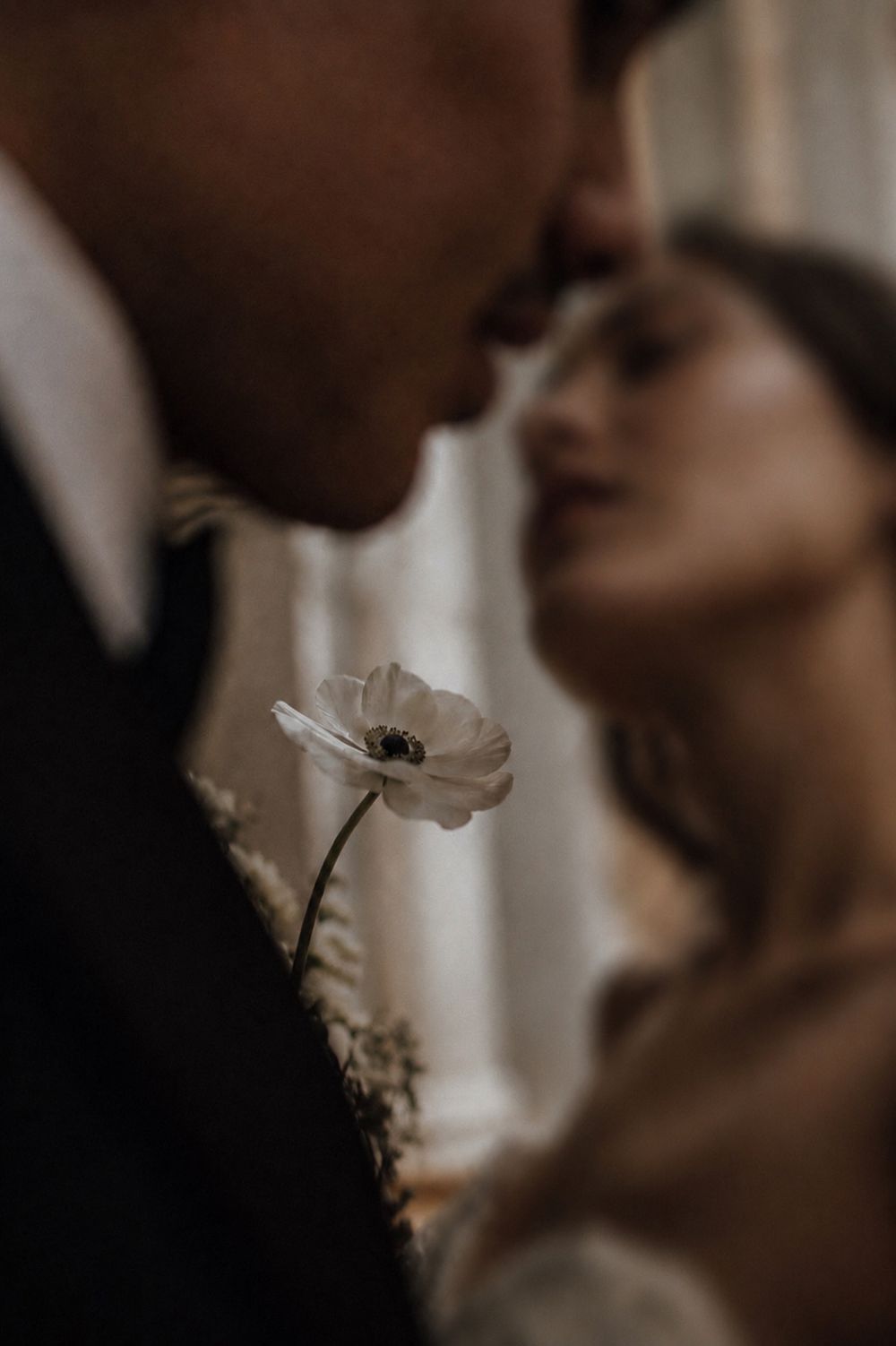 Couple nearly kissing with a white anemone in sharp focus at their wedding in Valle de Guadalupe, Baja.