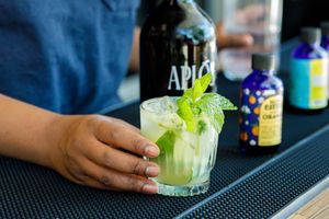 A bartender garnishes a mojito cocktail with fresh mint leaves on a black bar mat.