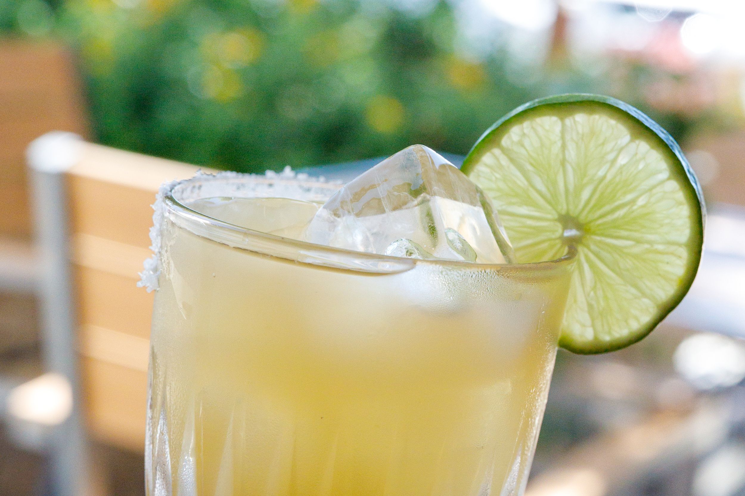 A refreshing margarita cocktail with ice and a lime wheel garnish served in a glass with a salted rim.