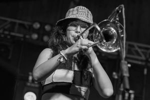 Black and white photo of a musician playing trombone on stage with concert lighting visible in background.