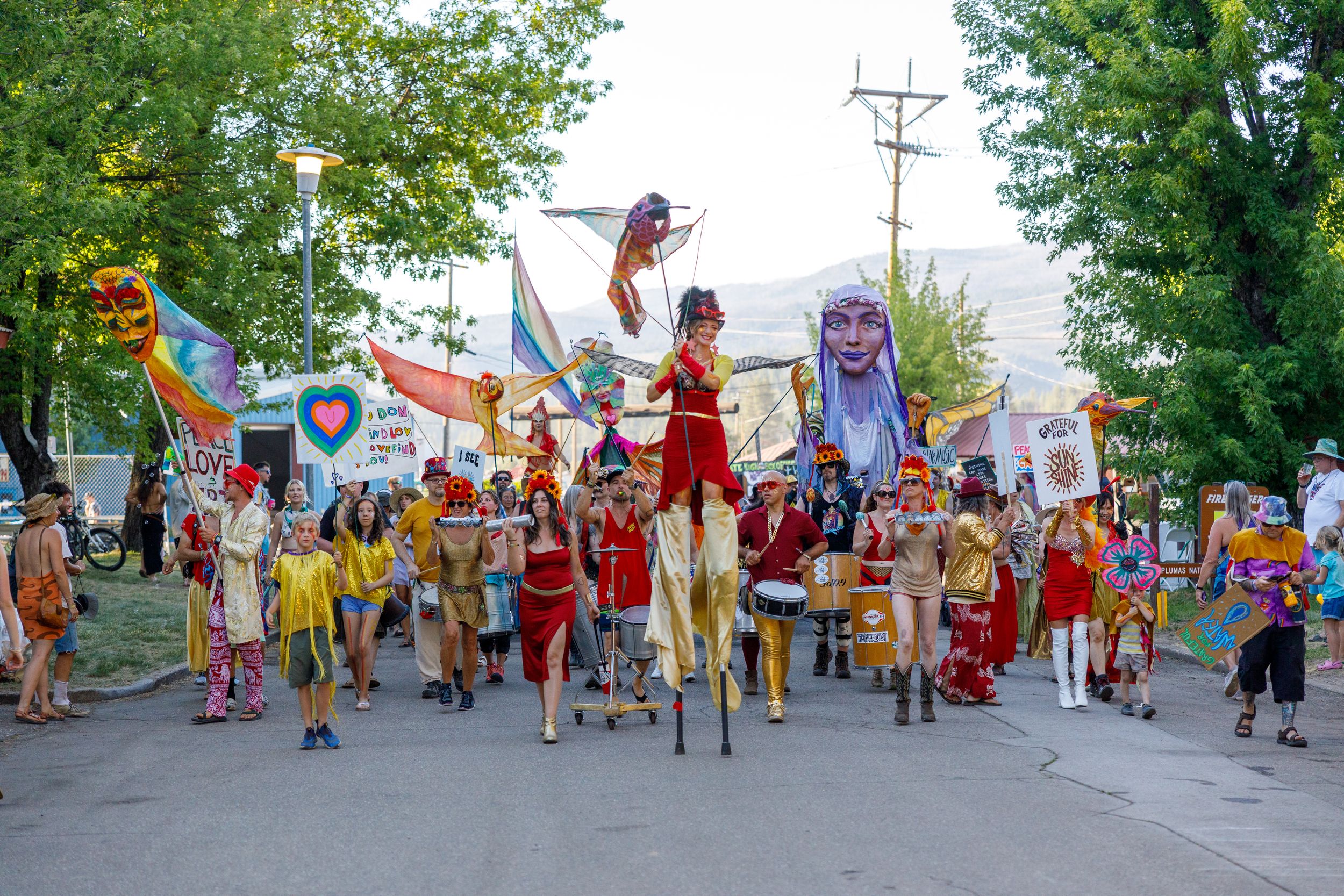 A colorful parade of performers on stilts marches down a street during a festival celebration with banners and props.