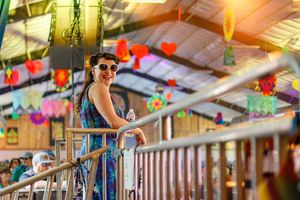 A performer leans on a railing under colorful decorative lights at a festival venue.
