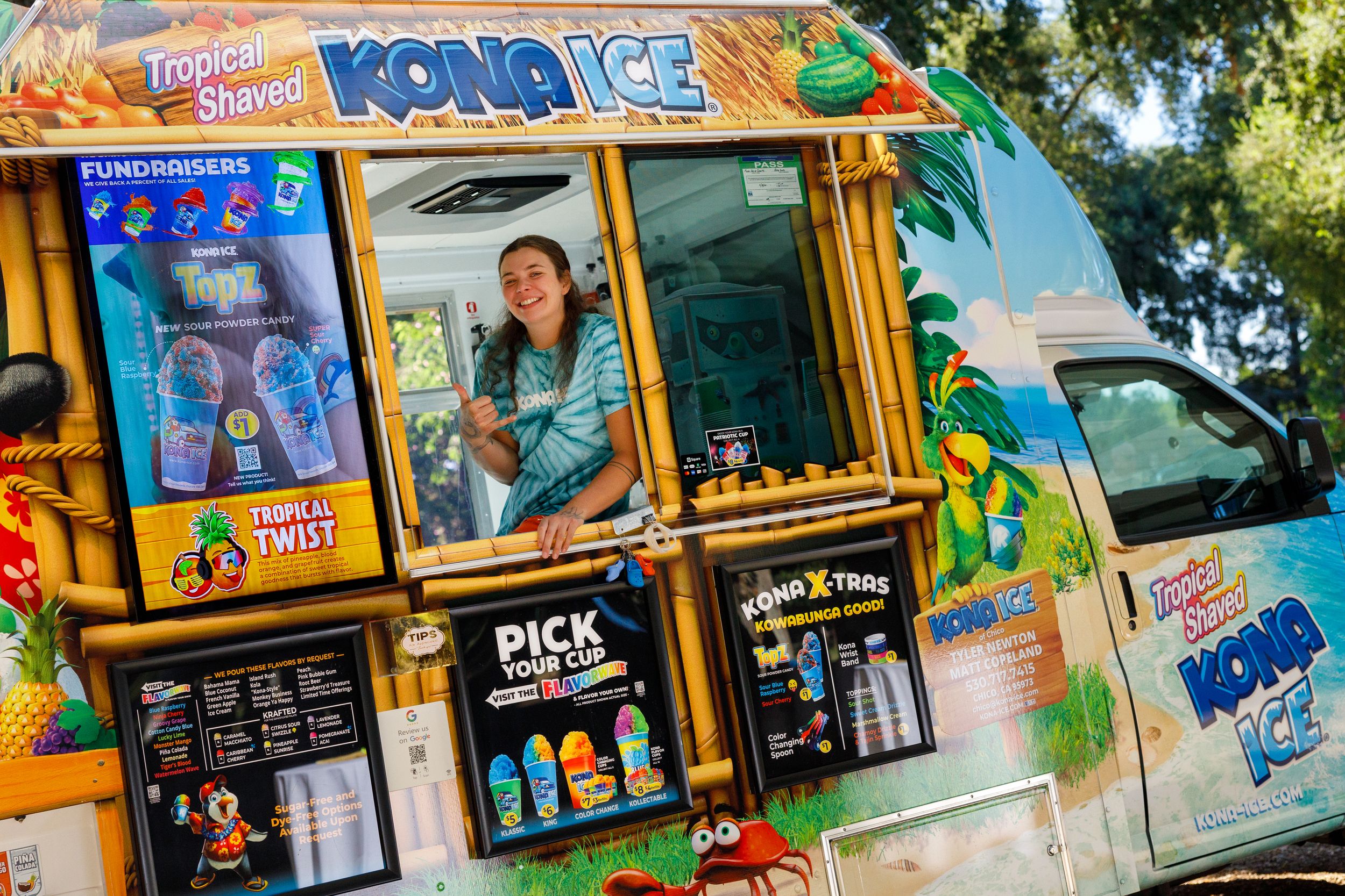 A colorful Kona Ice shaved ice food truck with tropical decorations and snack menu displays on a sunny day.