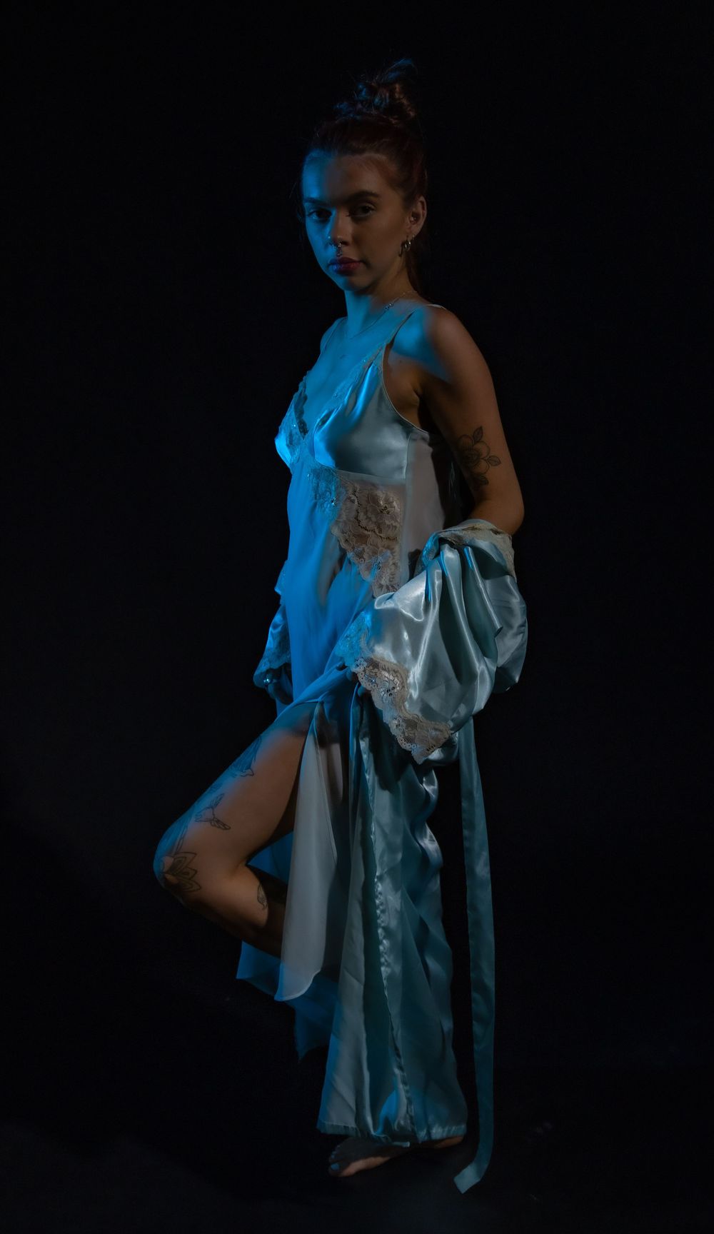 Artistic fashion photo showing flowing white silk dress illuminated by dramatic blue lighting.