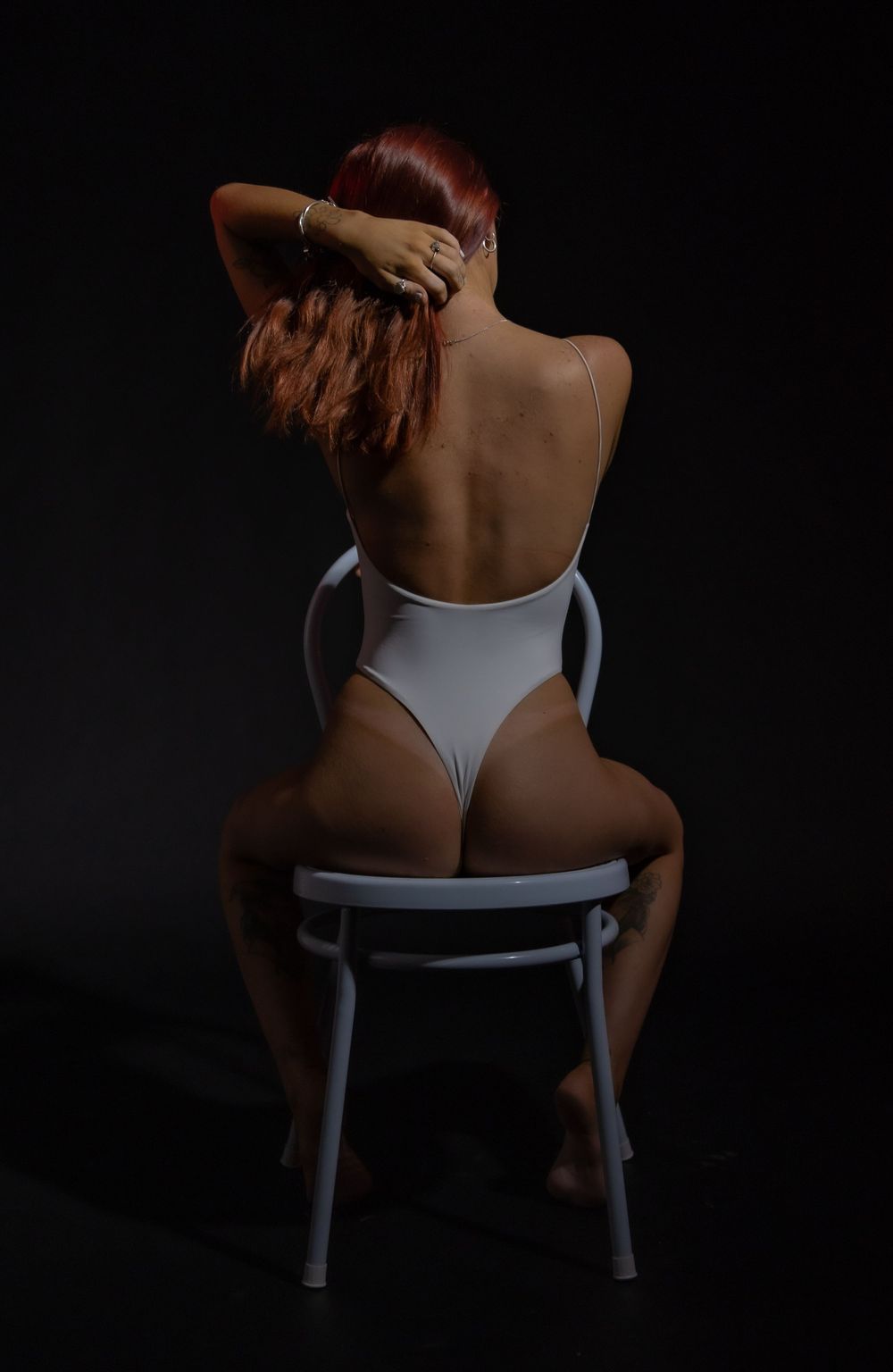 Artistic series showing dancer in white top on chair against dark background with dramatic shadows.