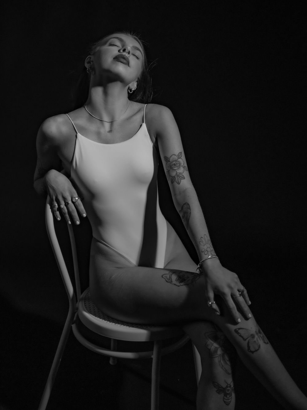 Dramatic monochrome studio image featuring white tank top and artistic pose on chair.