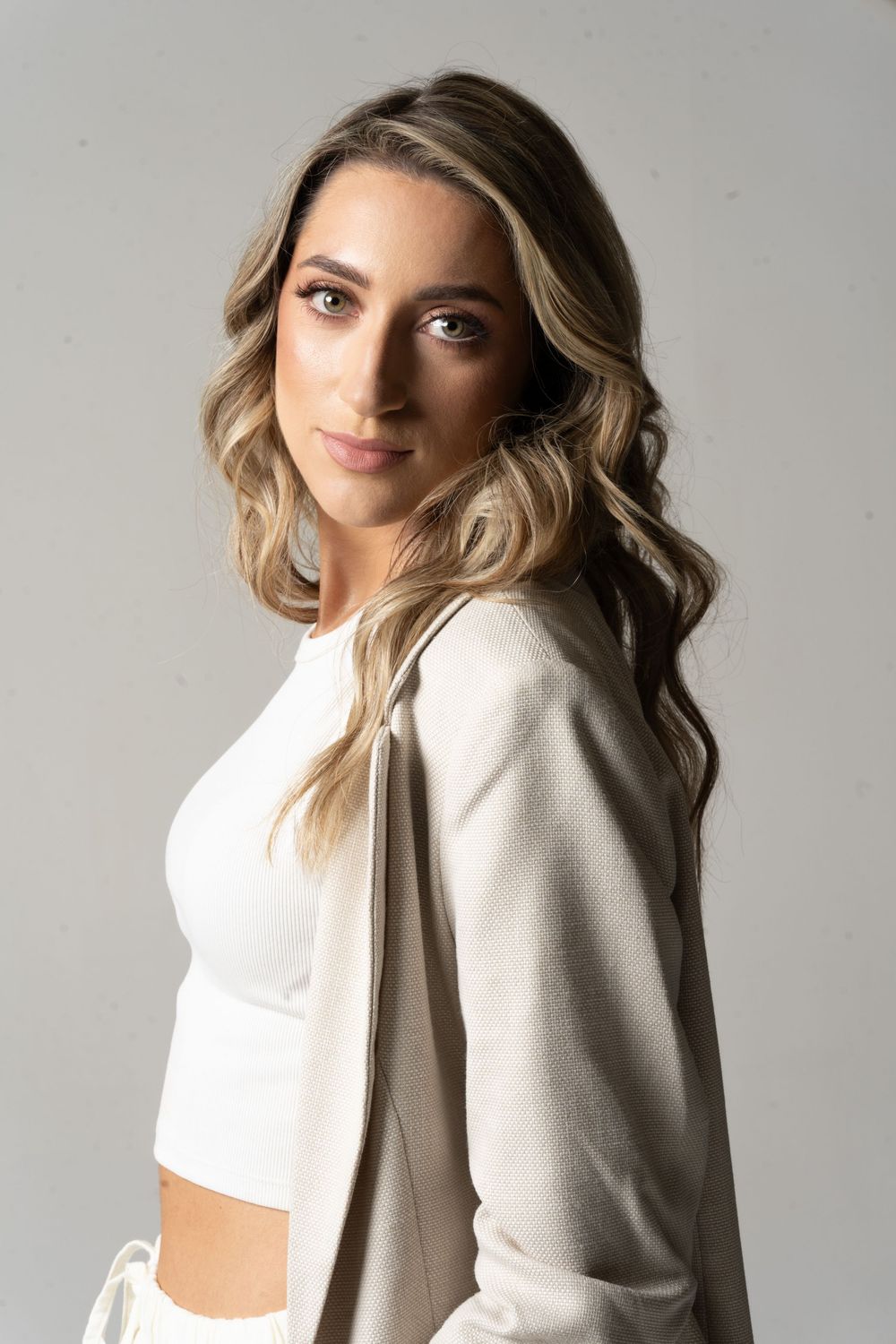 Elegancka kobieta w białym garniturze pozuje w studio. Portret biznesowy oświetlony ring light.