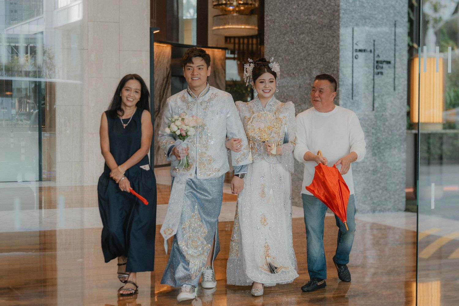 Group photo of wedding party in formal attire at modern venue entrance.