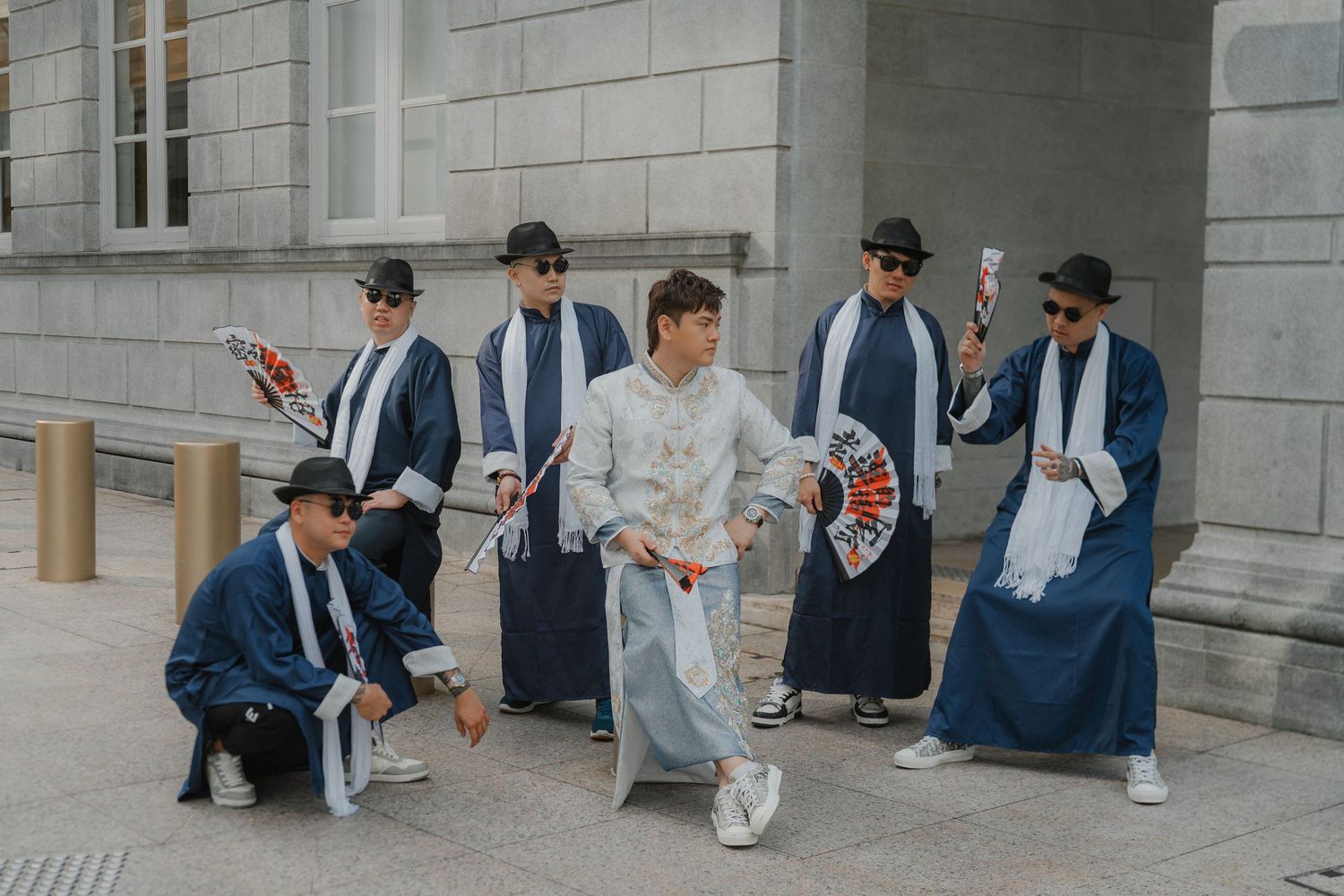 Groomsmen in dark blue suits gather together outside a stone building for a formal wedding photo.