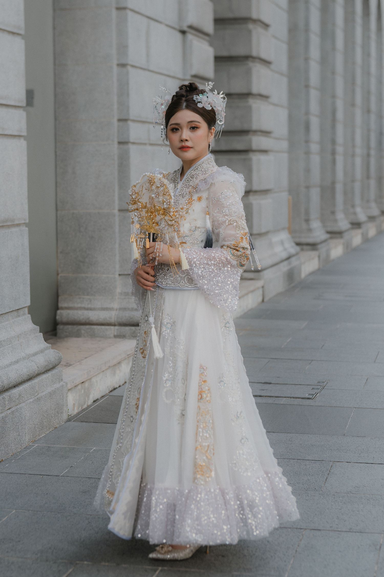 Elegant white lace wedding dress with long sleeves and intricate beading details photographed against classic stone columns.