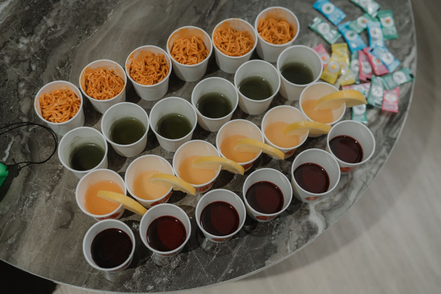 Rows of catering cups filled with orange and dark beverages served on a gray surface.
