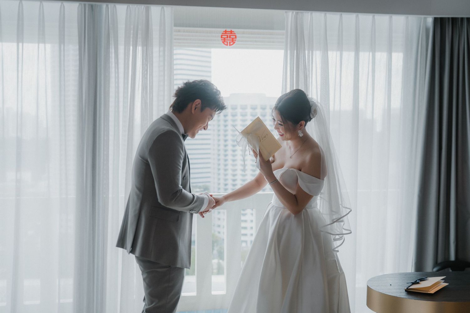 A couple in wedding attire share an intimate moment by sunlit windows during their wedding preparations.
