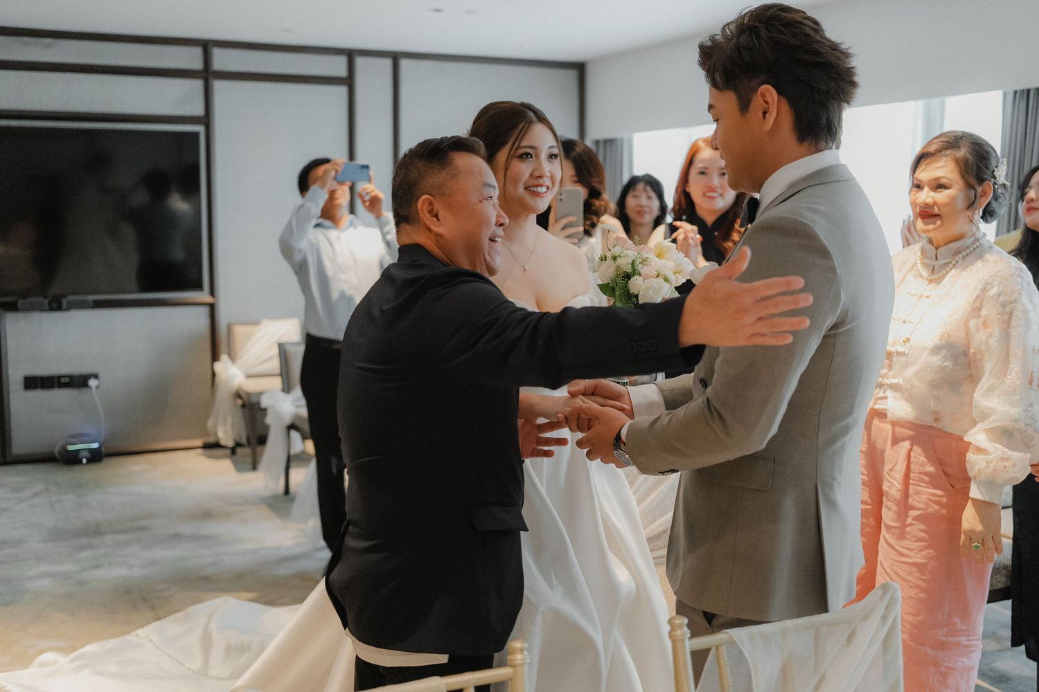 Two people share an emotional moment during a wedding ceremony while others look on in a bright indoor setting.