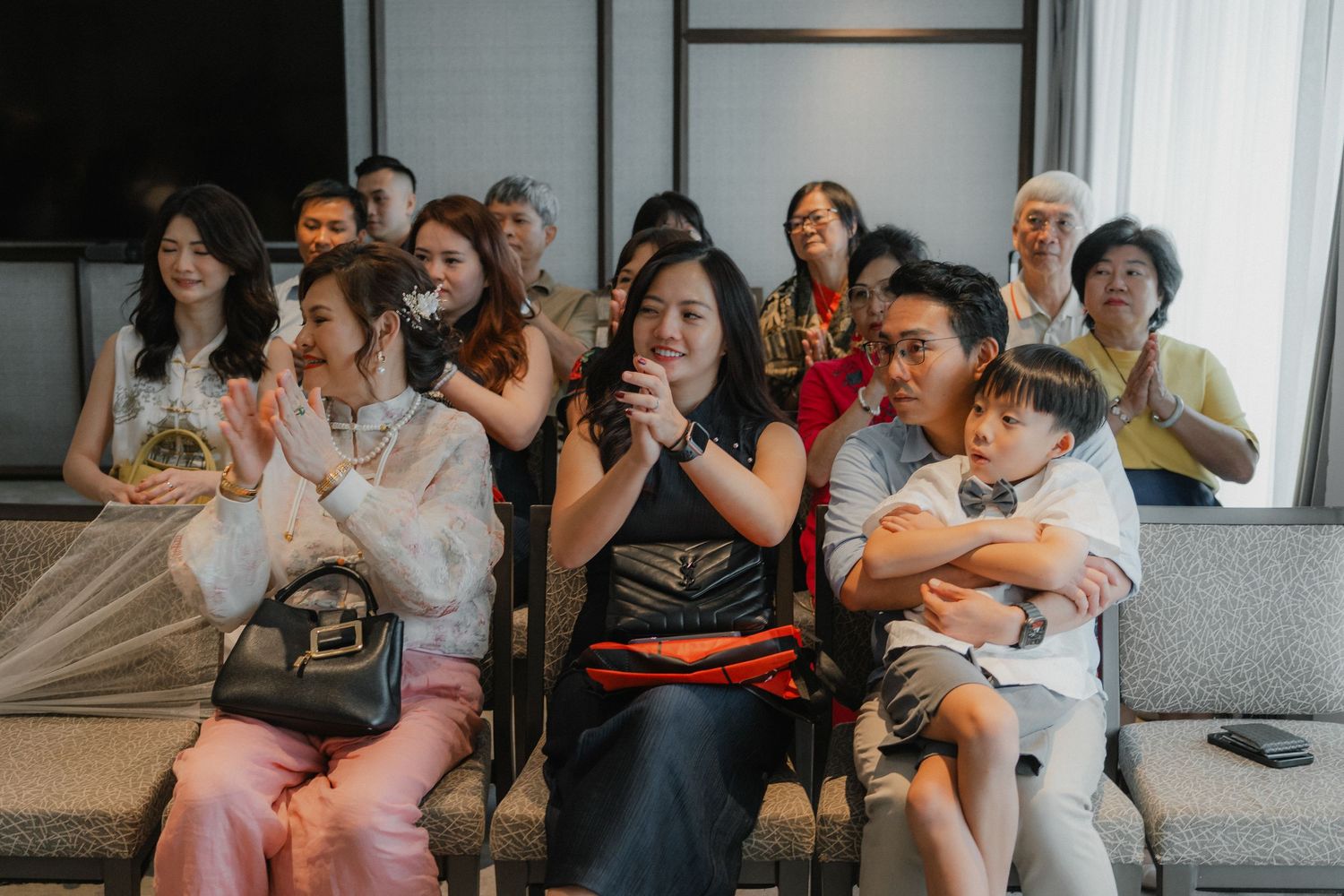 Wedding guests seated on modern grey couches watching an event unfold in front of them.
