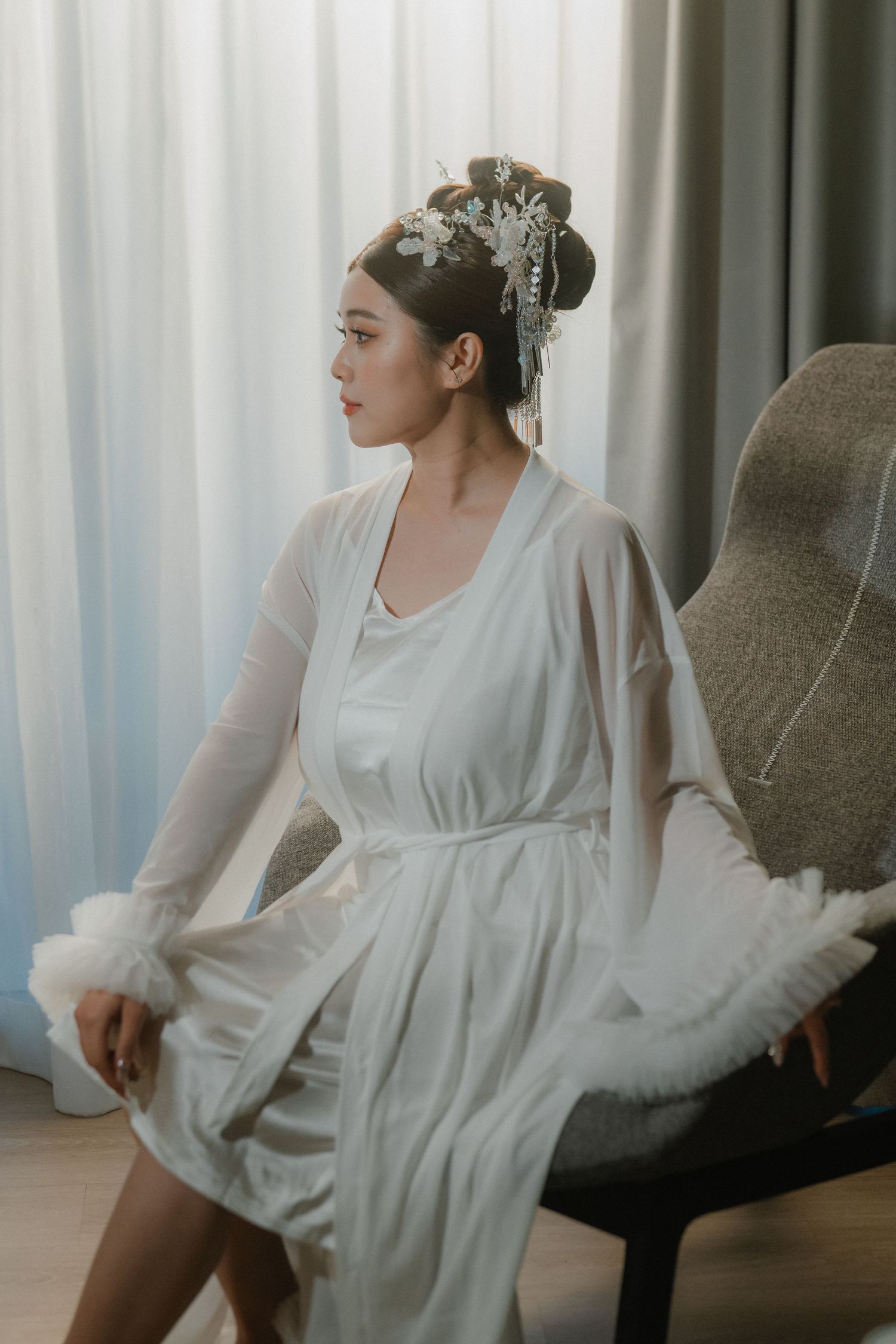 White bridal robe against curtained window during wedding preparations.