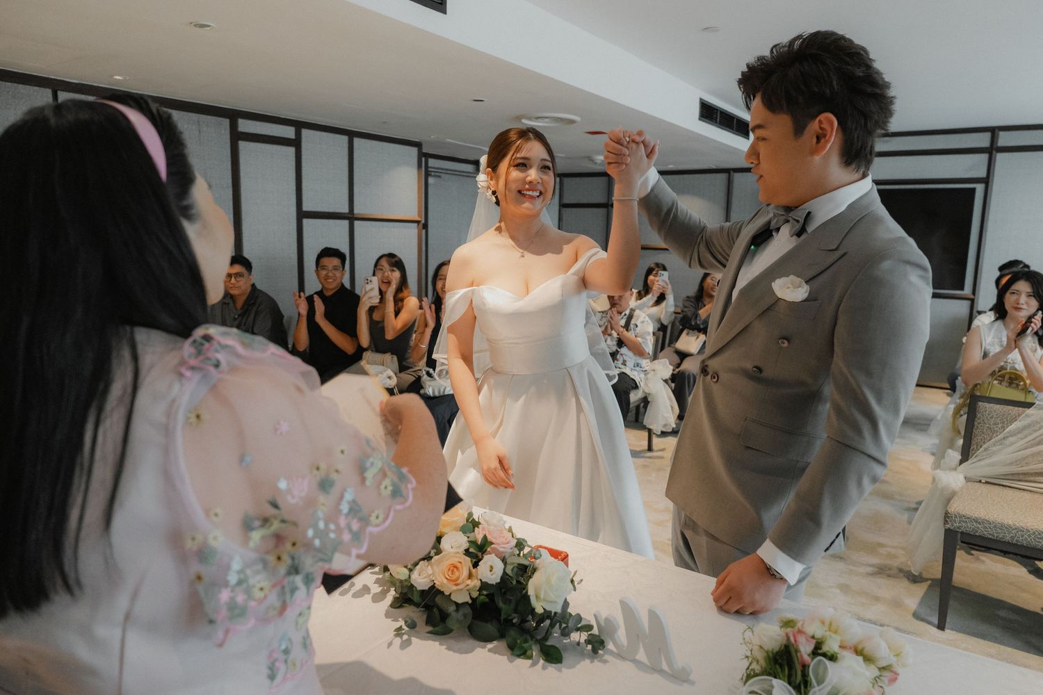 Couple stands at a modern minimalist indoor venue during their wedding ceremony as guests watch and take photos.