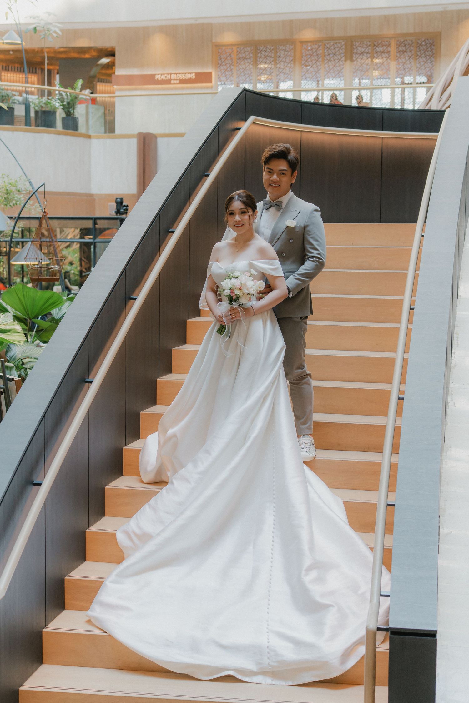 A flowing white wedding gown with a long train cascades down modern orange-tinted stairs.
