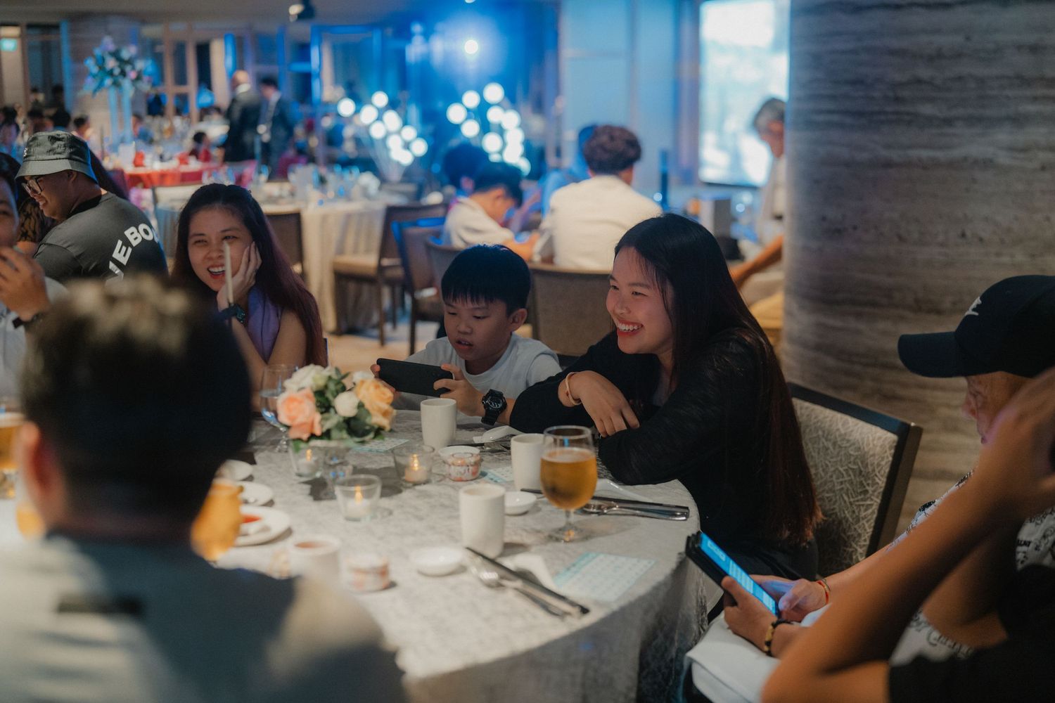 Guests enjoying a wedding reception dinner at round tables in a dimly lit restaurant setting.