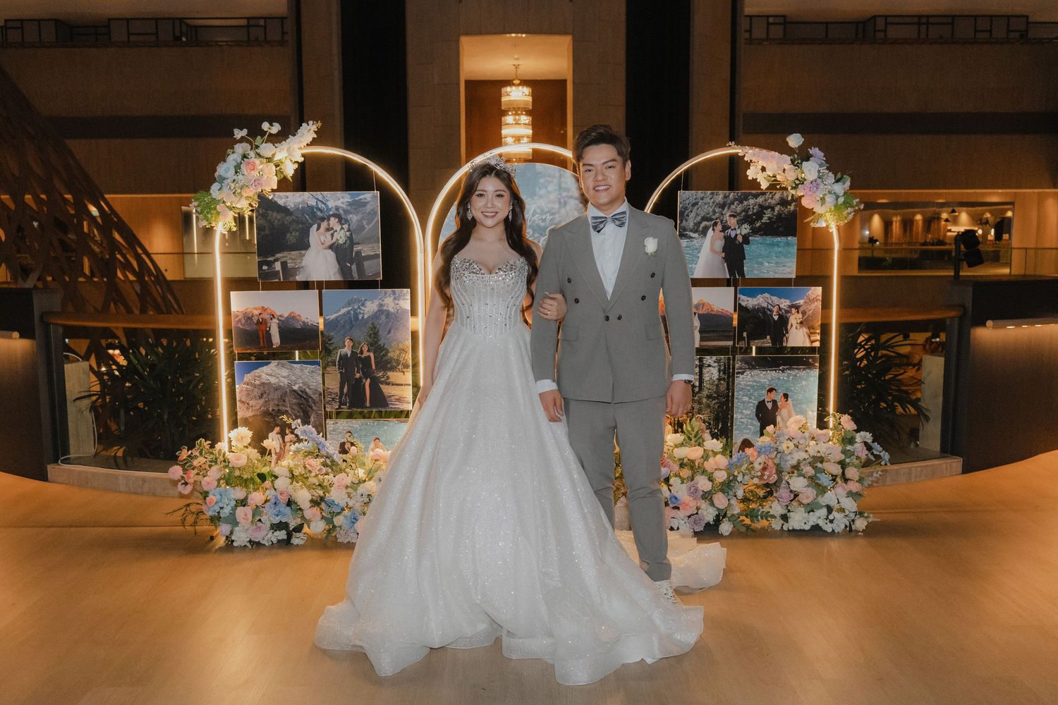 Elegant couple poses at wedding ceremony with golden arch and pastel floral arrangements in luxurious indoor venue.