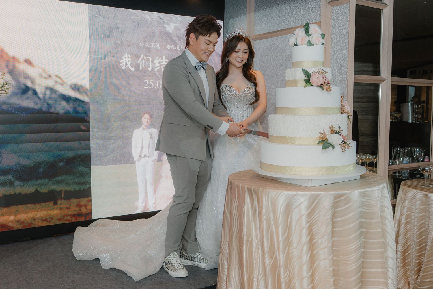 Elegant white wedding cake display on draped table with mountain backdrop.