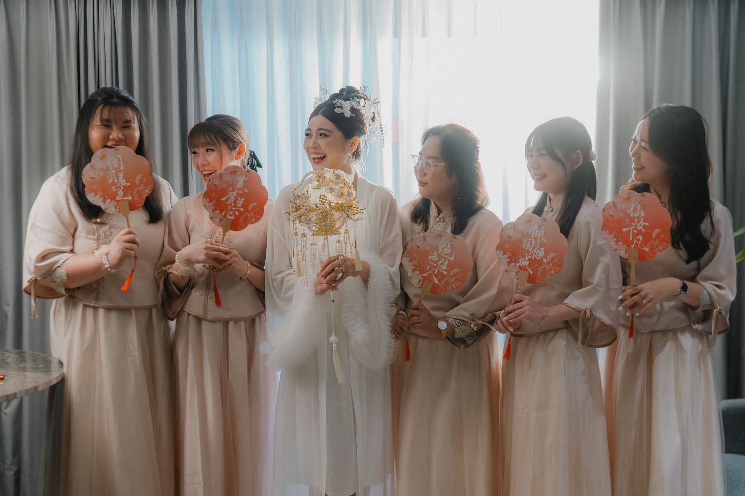 Bridesmaids in matching cream-colored robes stand together holding flowers.