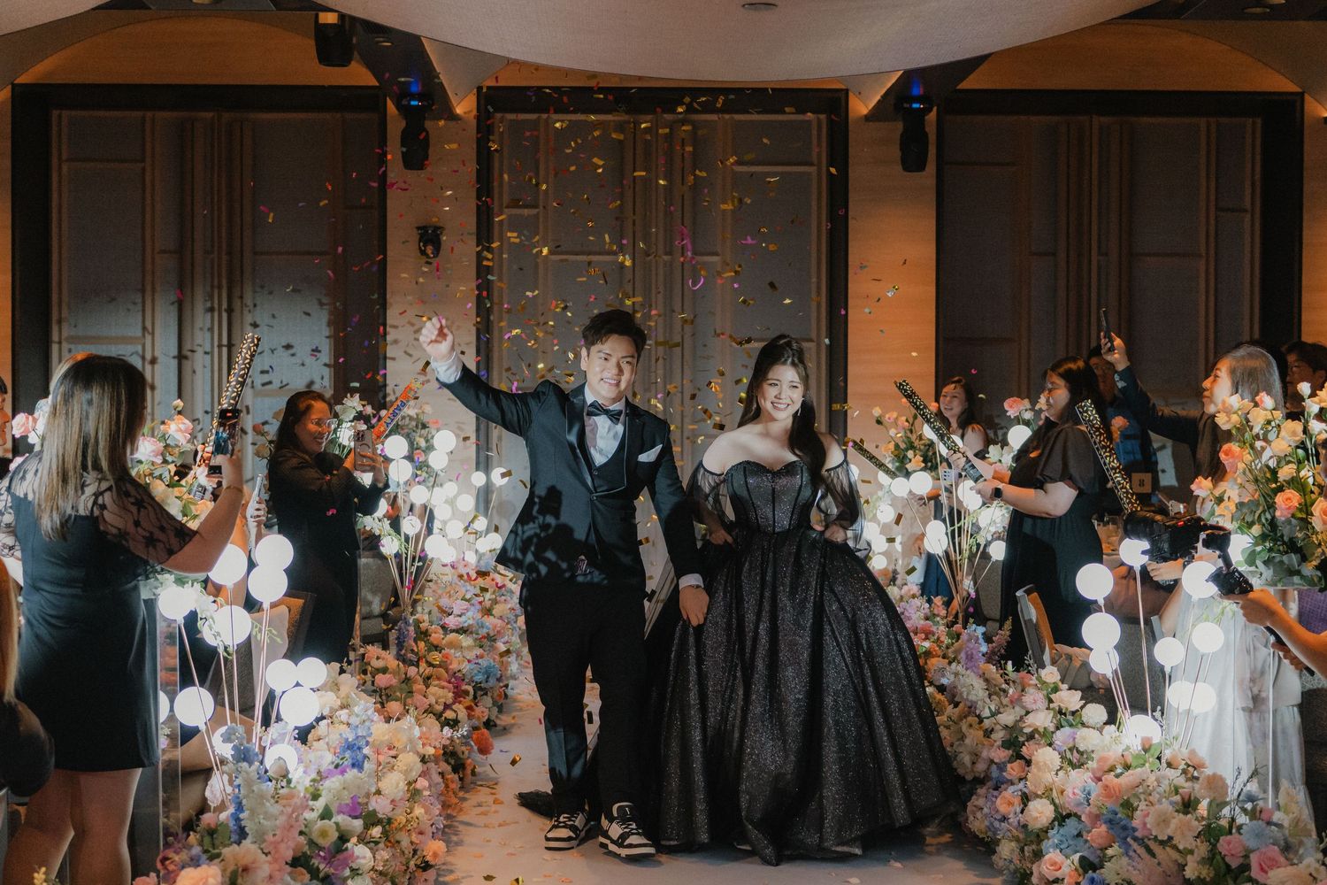 A wedding celebration with guests holding sparklers as a couple walks through in formal black attire.